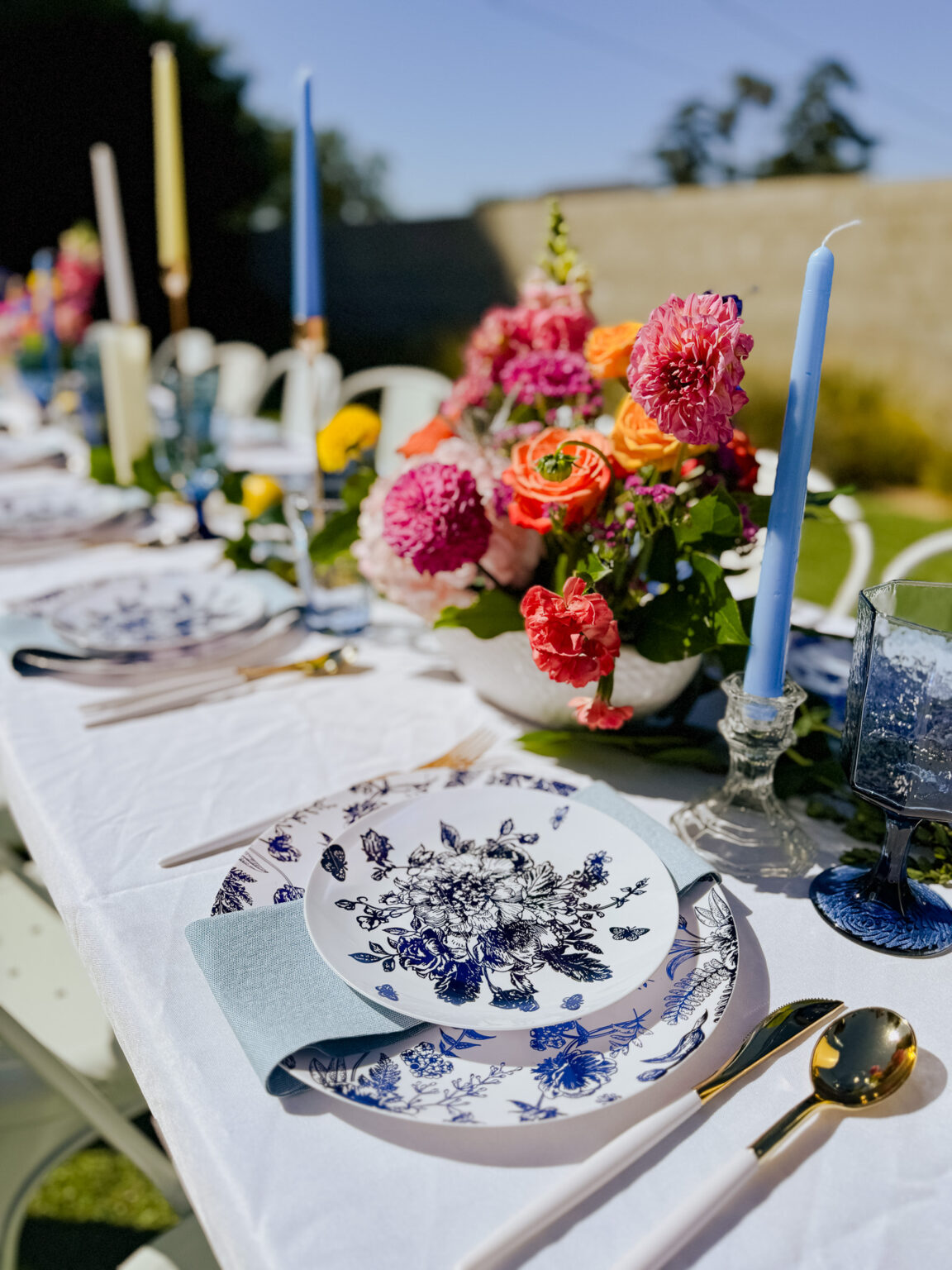Outdoor tablescape with blue-and-white floral china, gold flatware, taper candles and a bright dahlia centerpiece