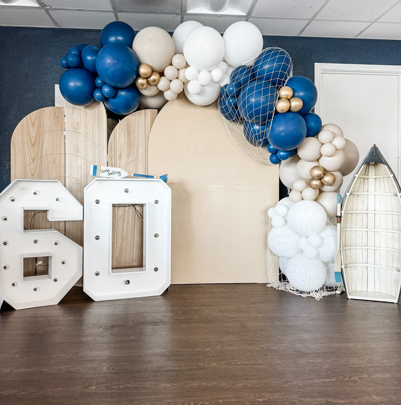 Marquee "60" letters in front of navy, white and gold balloons and wood arch panels for a 60th birthday