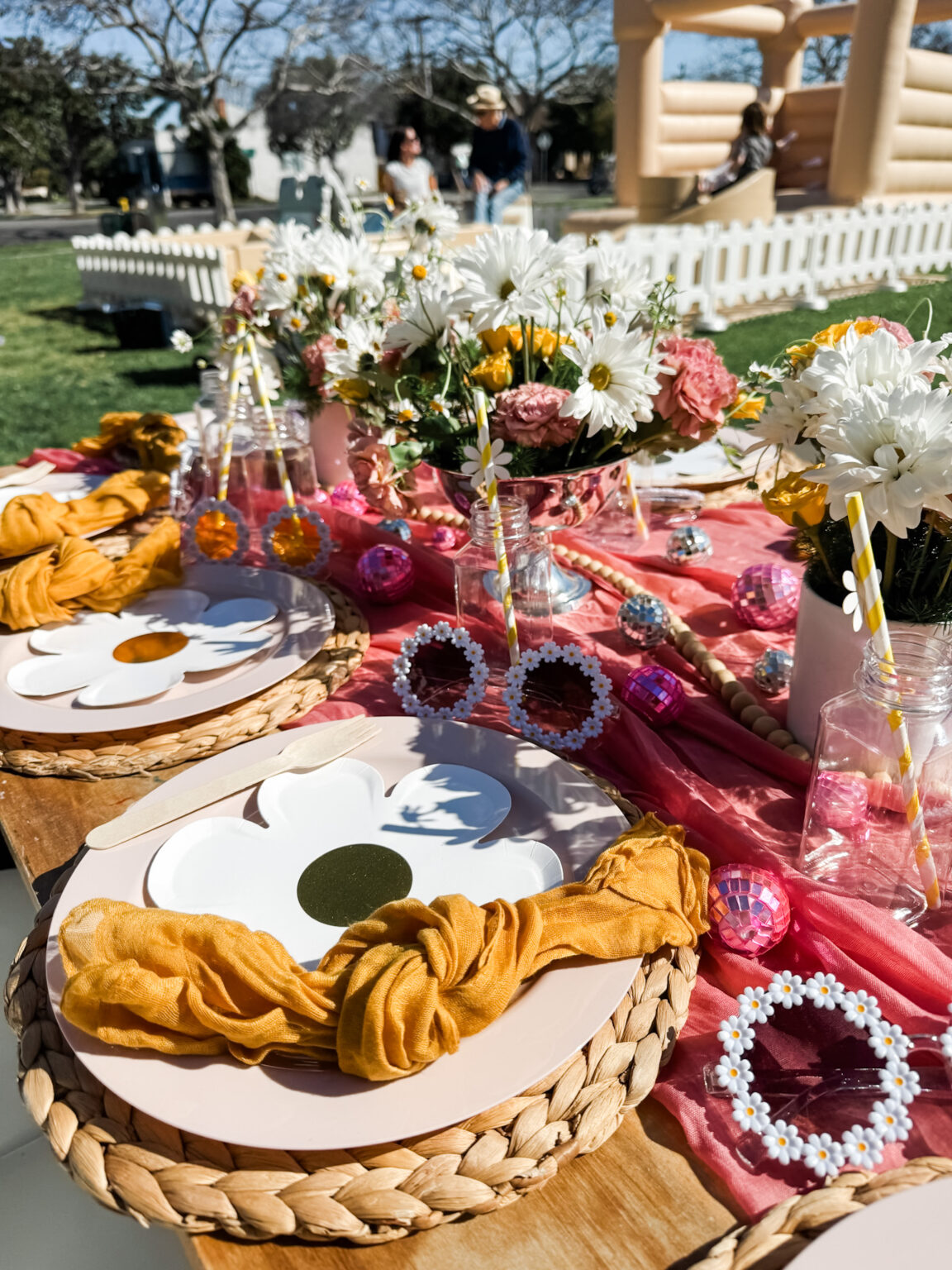 Boho tablescape with blush and mustard linens, woven chargers, pink glassware and fresh florals at an outdoor party