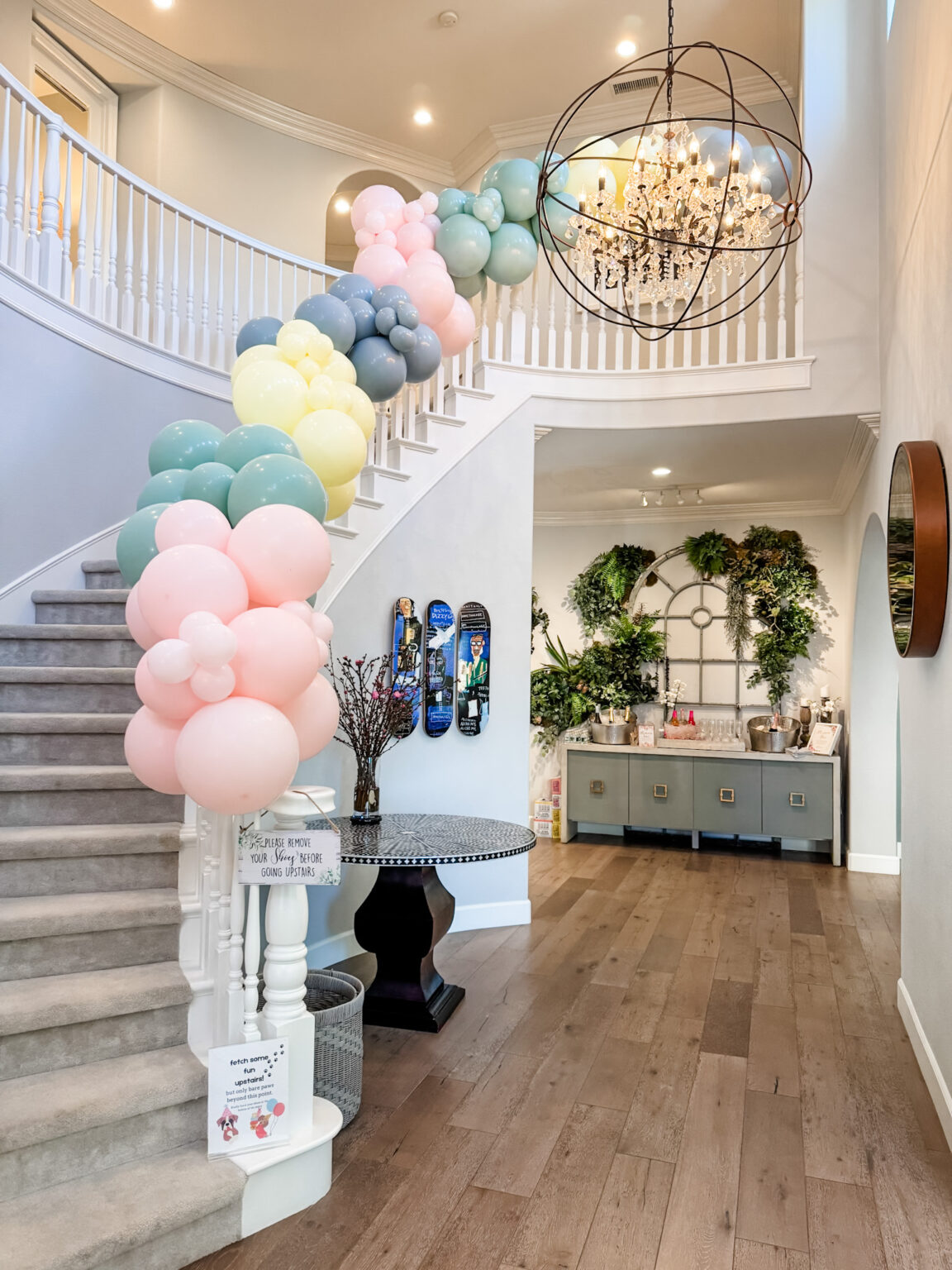 Pastel balloon columns in pink, yellow and sage lining a curved staircase in a bright San Diego home