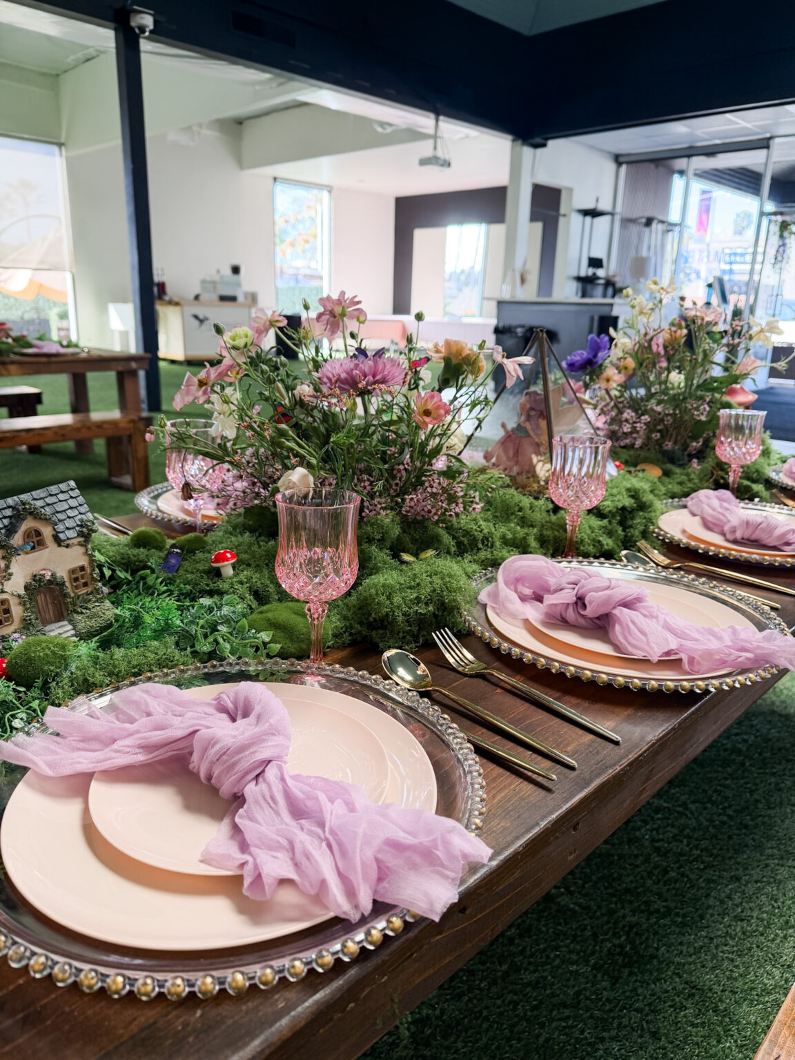 Lush garden tablescape with pink and white florals, blush napkins, gold-beaded chargers and pink glassware under a covered patio
