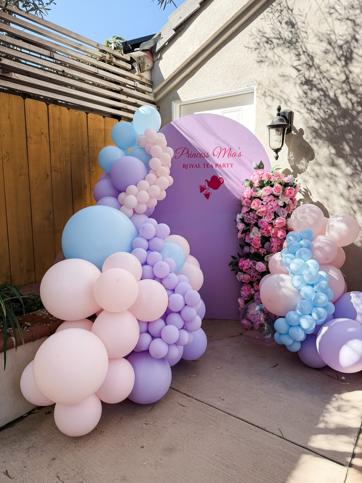 Pastel pink, lilac and baby-blue balloon garlands framing two arch panels with a fresh floral accent
