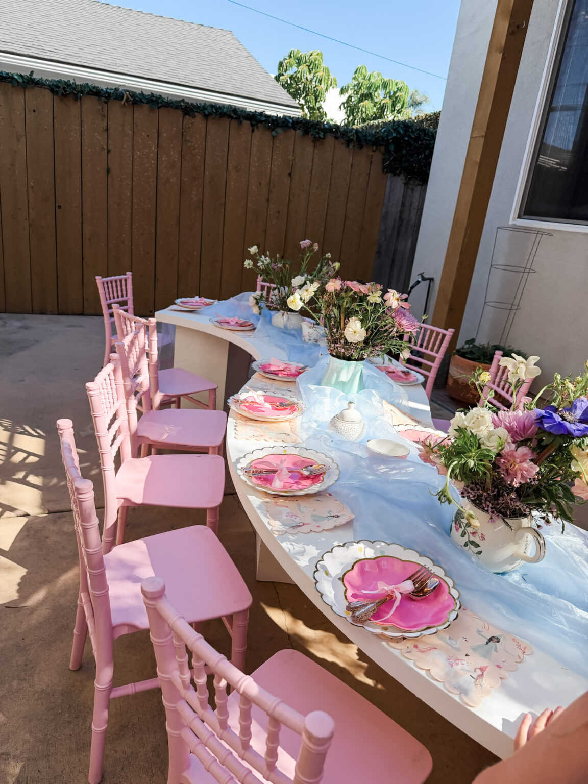 Garden tea party table with pink chiavari chairs, fresh pink florals and pastel place settings