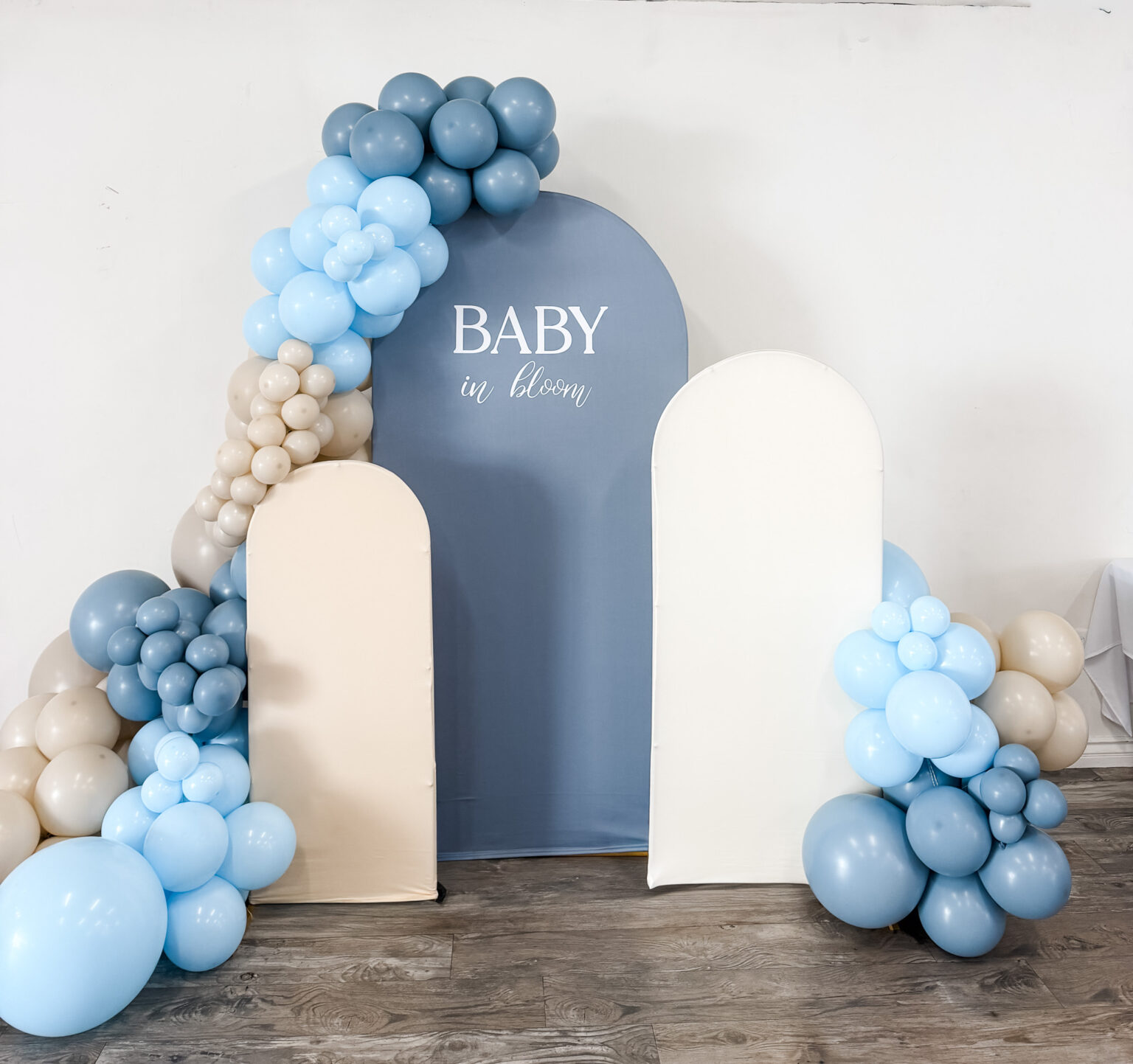 Baby shower installation with dusty blue and cream arch panels and a cloud-like blue, white and taupe balloon garland