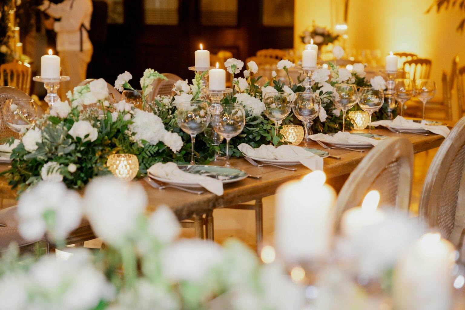 Candlelit wedding dinner table with white florals, glassware and folded napkins