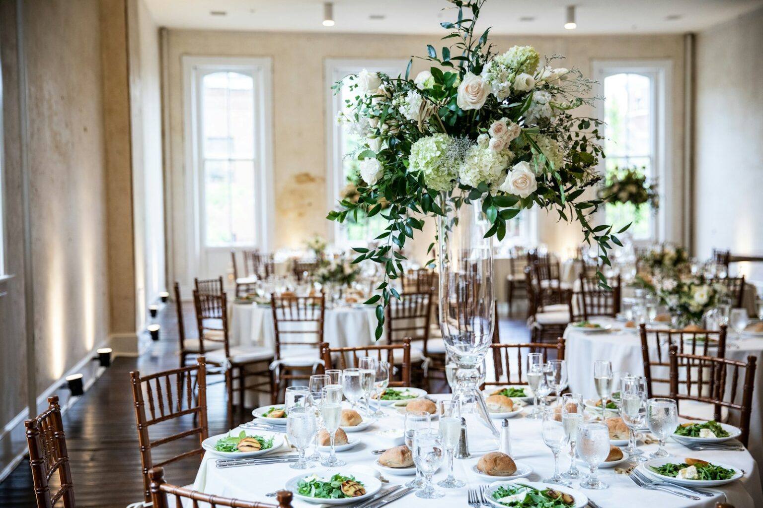 Wedding reception table with a tall white hydrangea and greenery centerpiece in a bright room